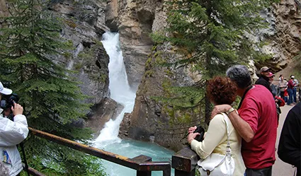 Tourists taking pictures of waterfall at Johnston Canyon in the Canadian Rockies, while on tour.