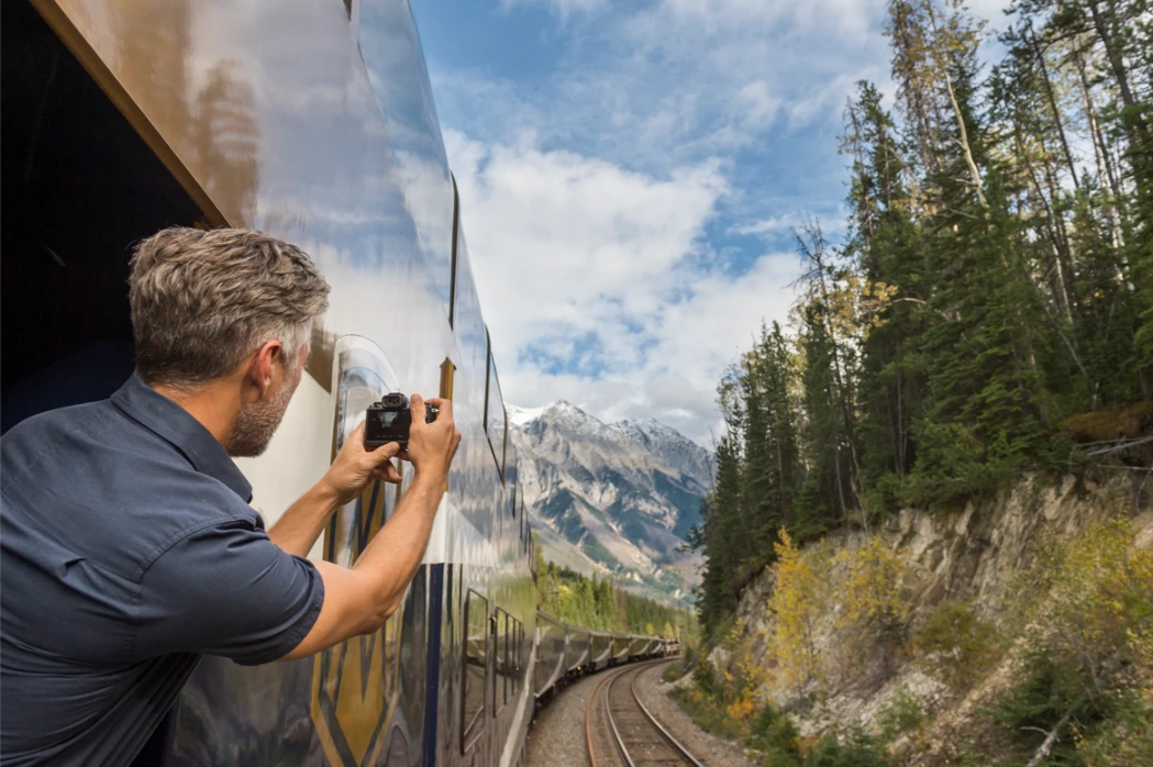 A man takes a photo of the approaching Rocky Mountains aboard the GoldLeaf Service viewing car.
